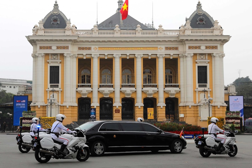 A black limousine surrounded by police motorcycles drives past the Hanoi Opera House.