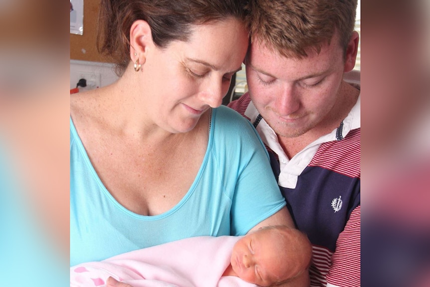 A man and woman hold a newborn baby in a hospital room.