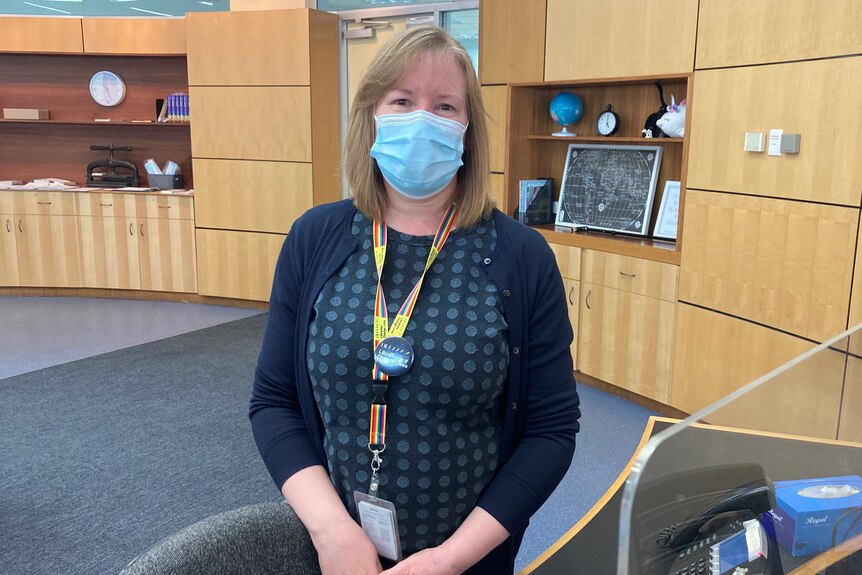 A woman standing behind a library desk with a COVID-19 mask on.