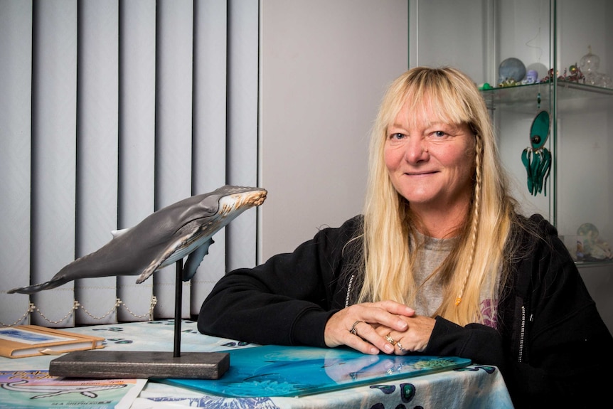 Jeannie Lawson kneels next to a model of a whale.