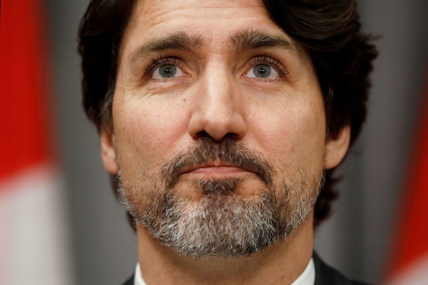 A close-up of a middle aged man in a suit with a beard, looking thoughtfully away from camera.