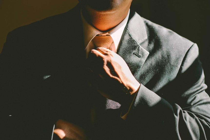 A man is putting on his suit depicting the stress that a secret workplace relationship can place on both parties