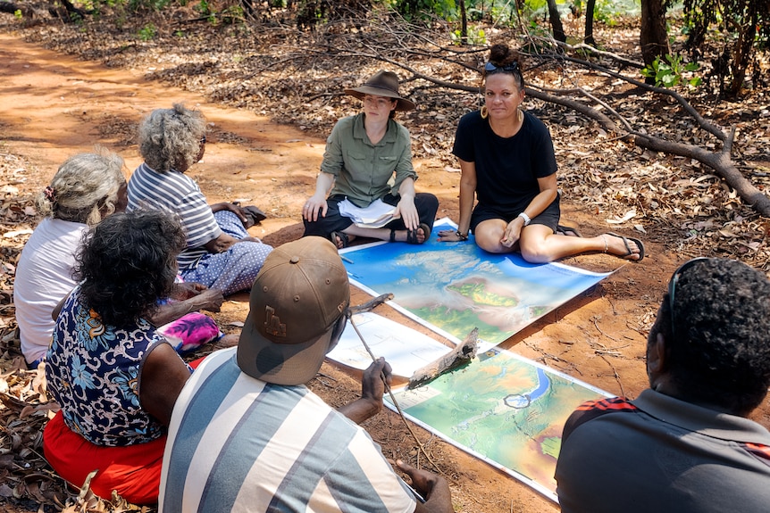 People sit around a large map laid out on a red dirt trail.