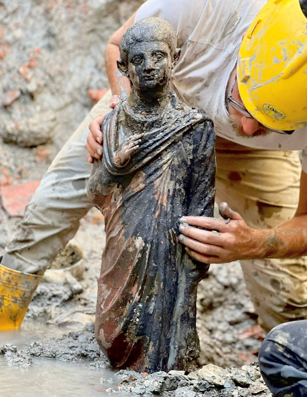 Un muncitor curăță o statuie de bronz găsită la un șantier de săpătură