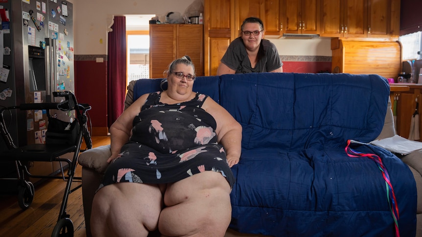 woman with very swollen legs sits on a couch with her daughter standing behind her