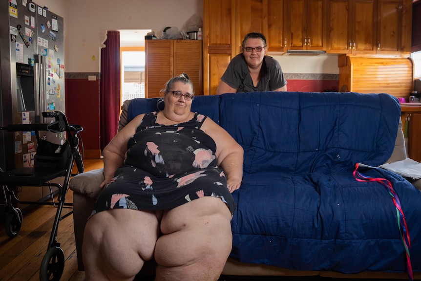 woman with very swollen legs sits on a couch with her daughter standing behind her