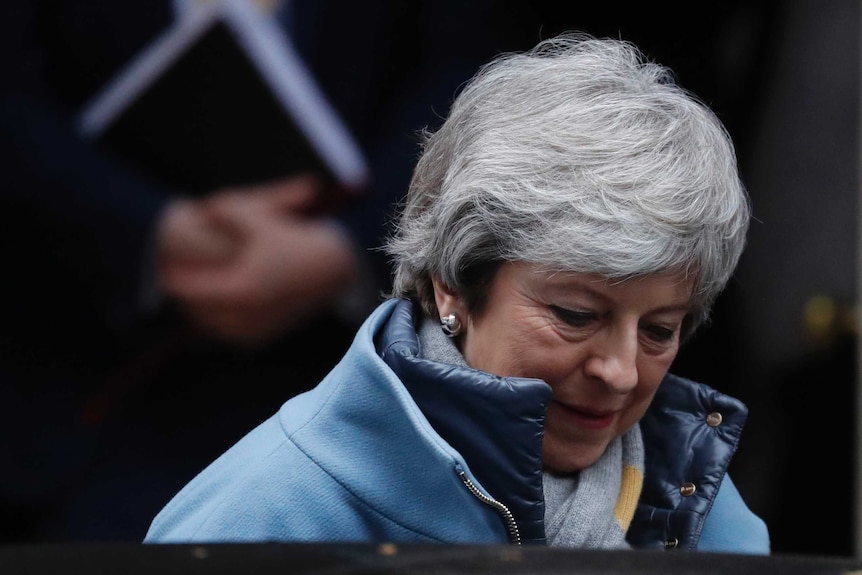 British Prime Minister Theresa May wears a heavy blue coat, her eyes downcast