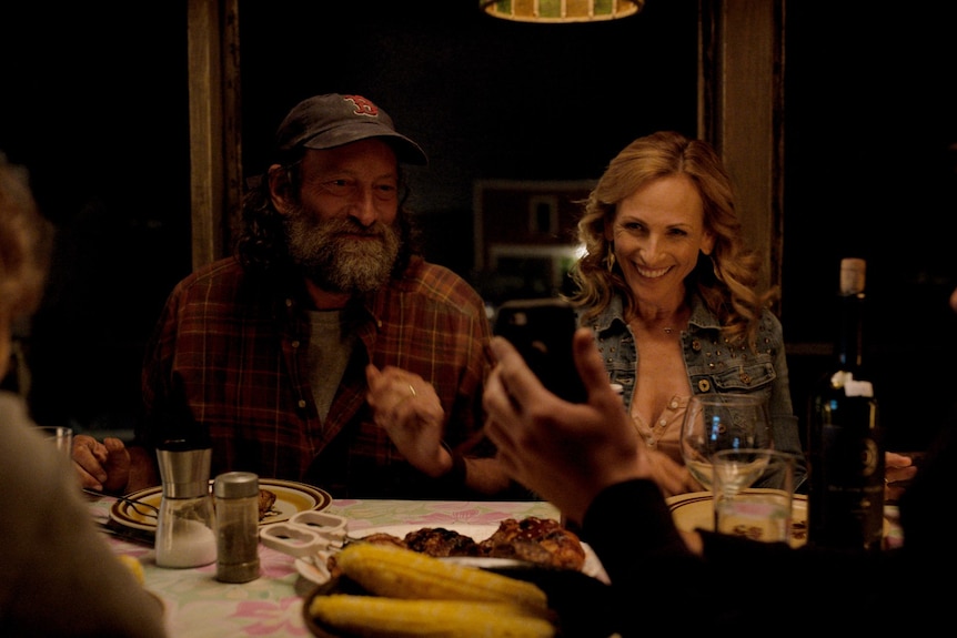 Une famille de quatre personnes, dont une fille et un fils adolescents, est assise en souriant et en riant à la table du dîner