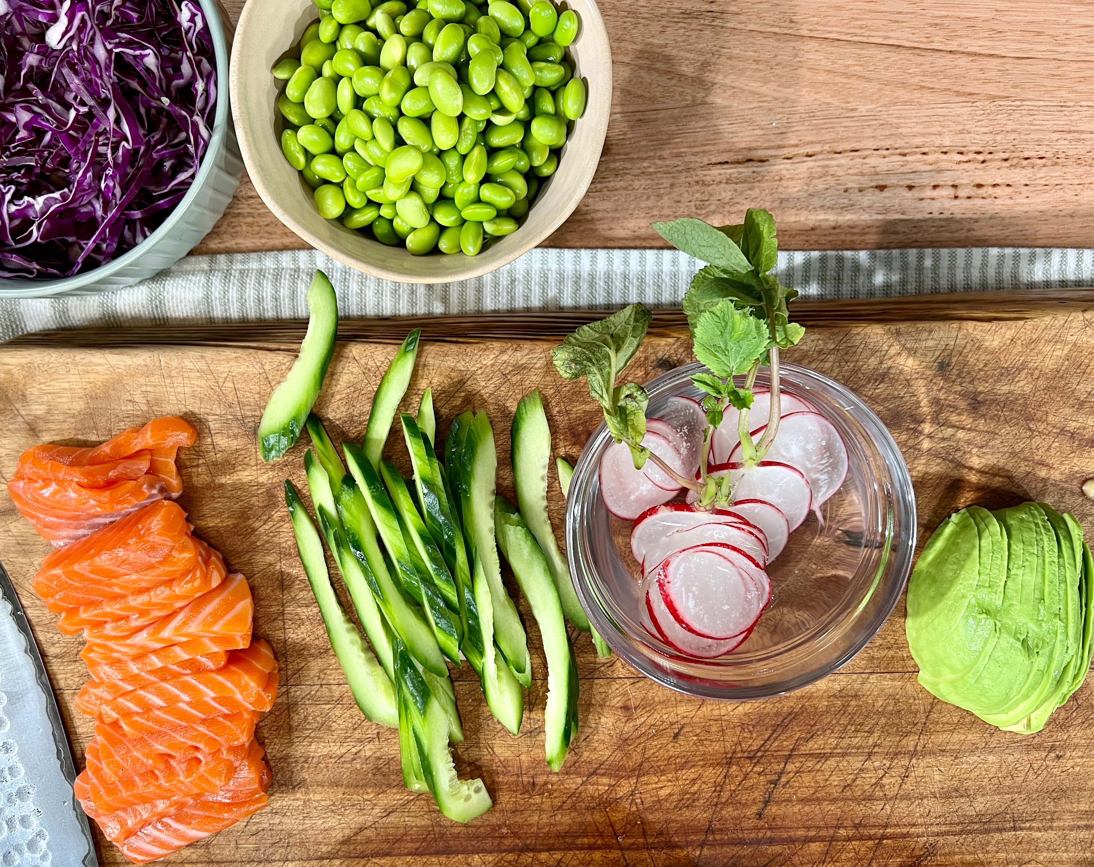 A picture of chopped salmon, avocado, radish, zucchini, beans and red cabbage on a chopping board.