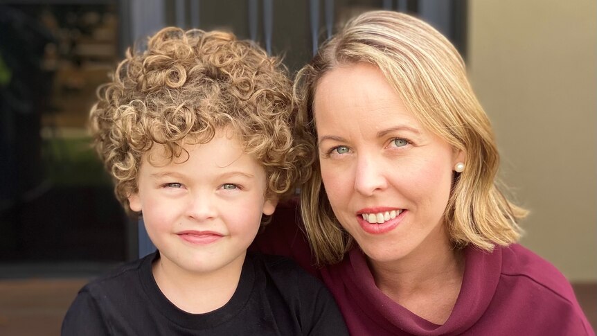 A young boy with curly hair next to his mum.