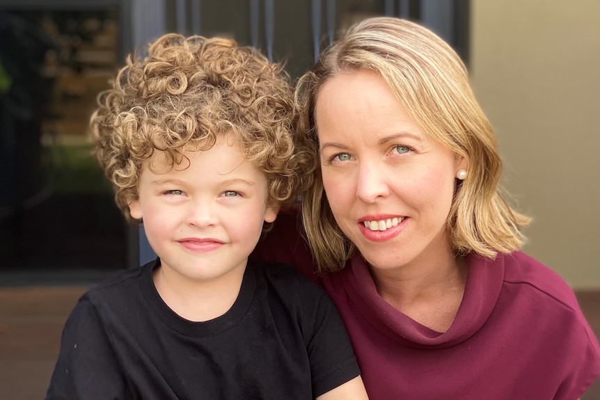 A young boy with curly hair next to his mum.