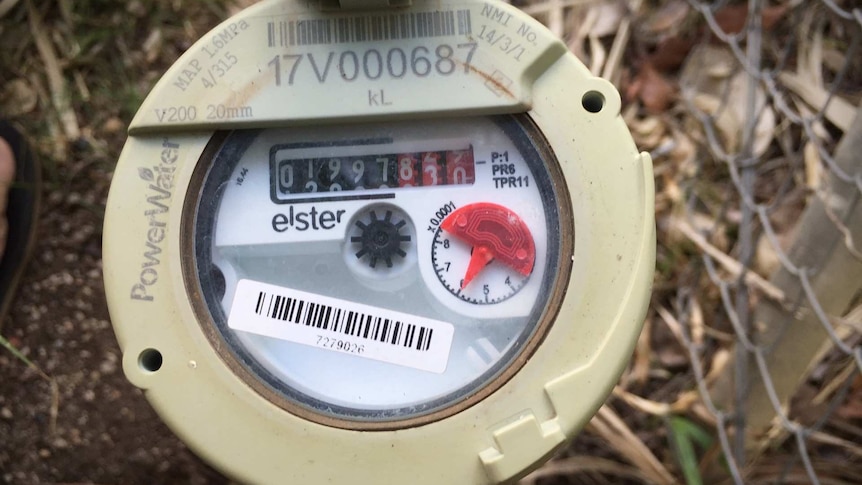 A close-up top view of a mains digit tally counter water meter outside a suburban home.