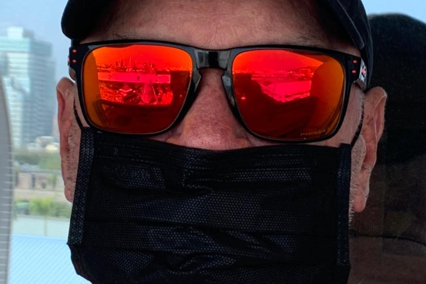 David Holst wearing a black cap, black and red sunglasses and a black face mask over his nose and mouth