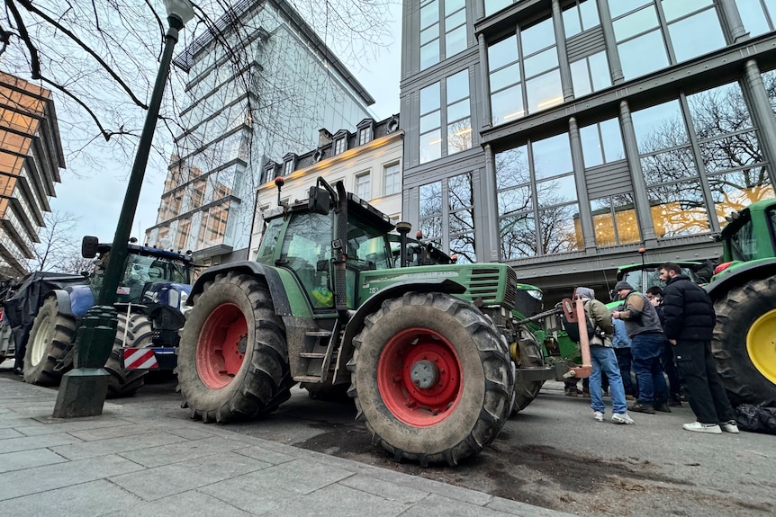 Large tractors parked outside tall buildings in a city.