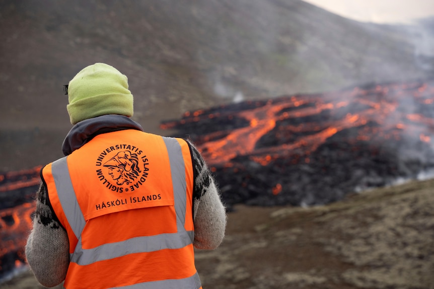 Man in beanie and hi vis stands in front of eruption Icelandic vocano 
