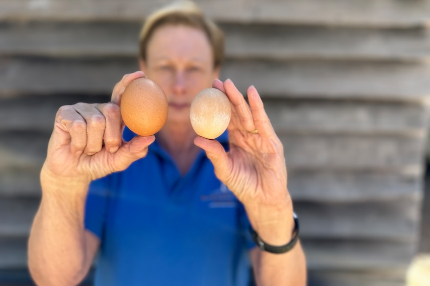 A woman holds up two eggs of different sizes.