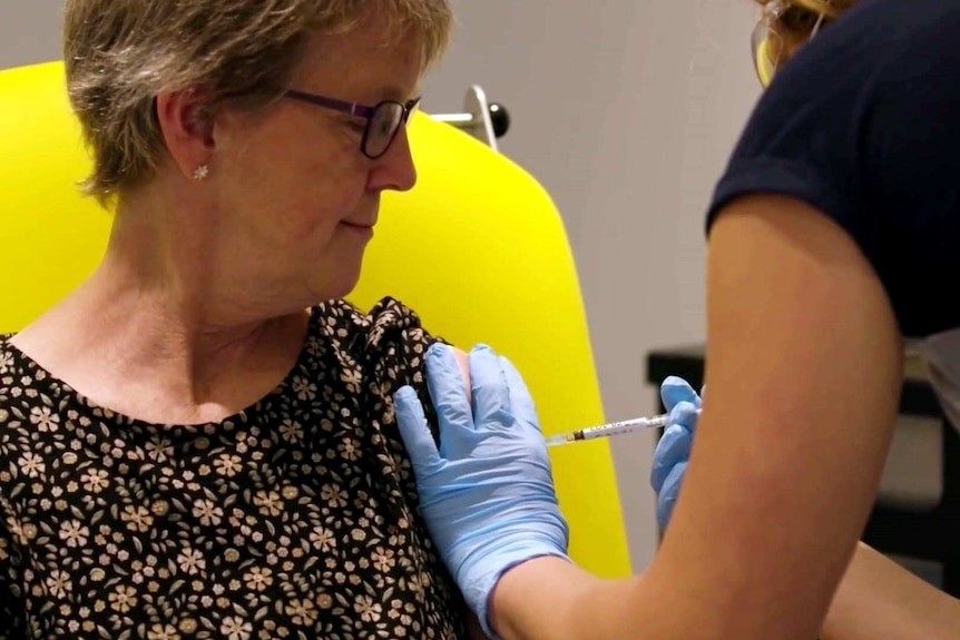 A woman looks at her arm as a nurse wearing gloves administers a vaccine