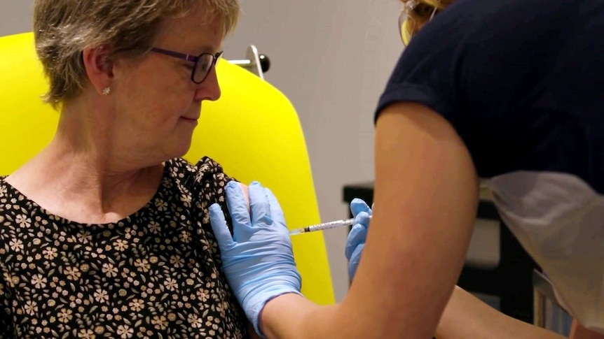 A woman looks at her arm as a nurse wearing gloves administers a vaccine