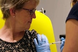 A woman looks at her arm as a nurse wearing gloves administers a vaccine