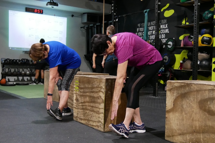 Two women stretching, leaning down to touch their toes.