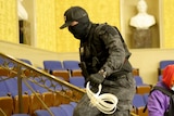 A masked man in military gear holds zip-tie handcuffs in the senate chamber of the US Capitol
