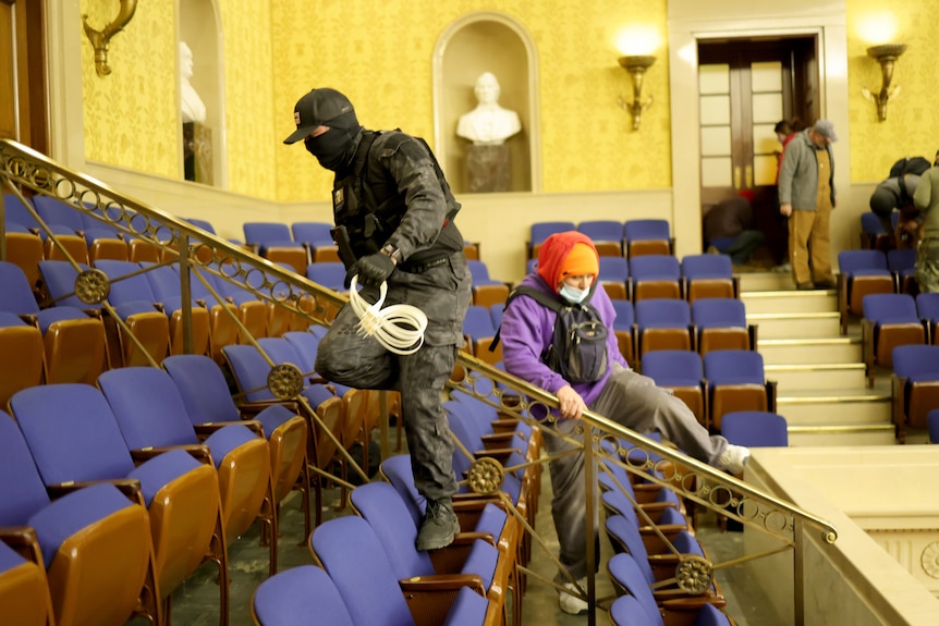 A masked man in military gear holds zip-tie handcuffs in the senate chamber of the US Capitol