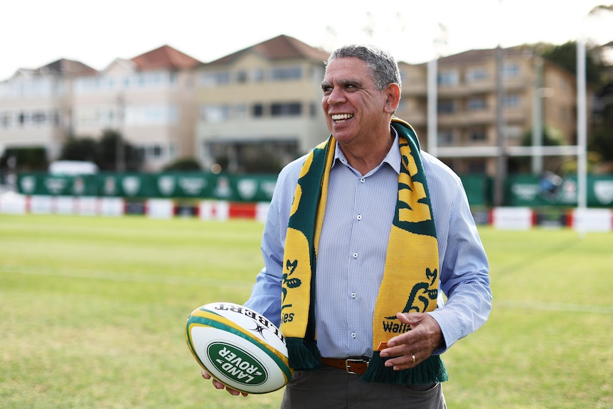 Mark Ella smiles while holding a ball and wearing a Wallabies scarf