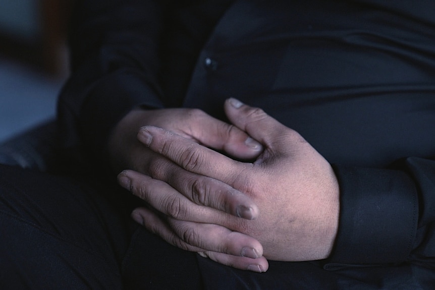 A man's hands are seen with his fingers laced together