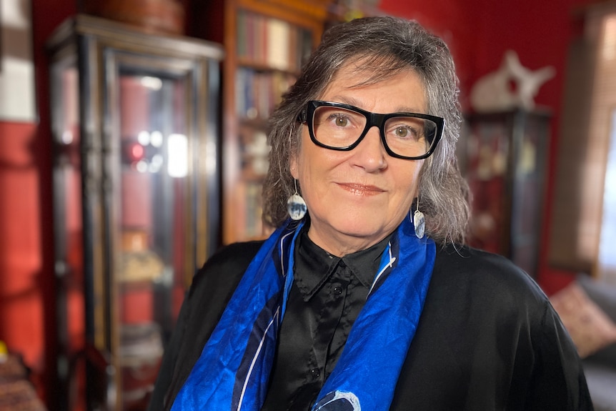 A woman wearing glasses stands inside an office.