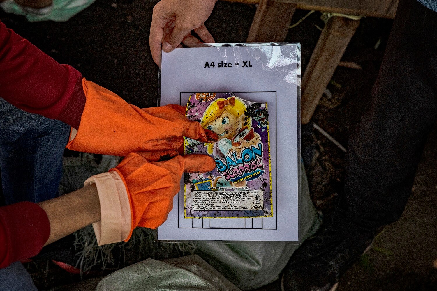 Close up photo of two hands holding a plastic sachet on A4 paper.