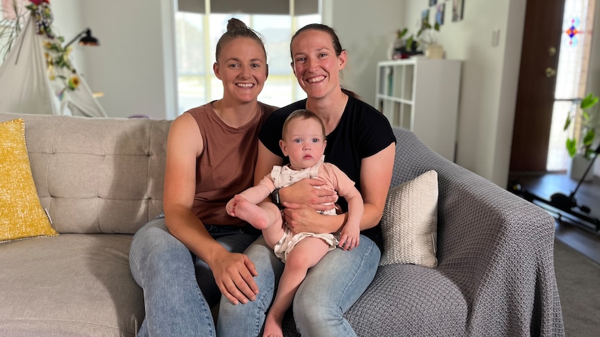 Two women sit on a couch holding their baby daughter