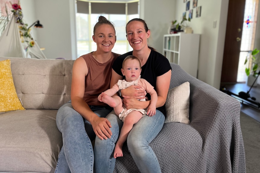 Two women sit on a couch holding their baby daughter