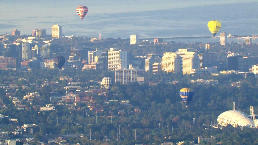 Hot air balloons over Melbourne's skyline under morning light.