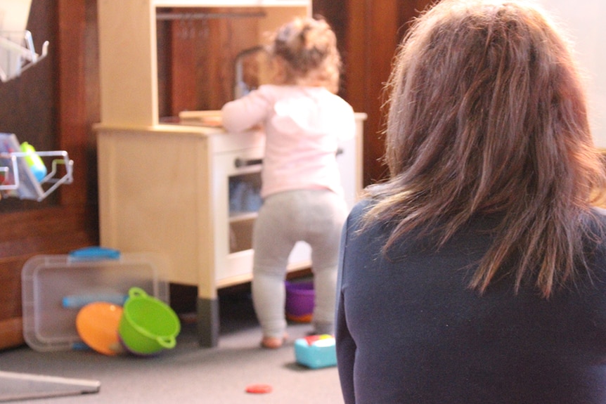 Young unidentified mother watches her female child play.