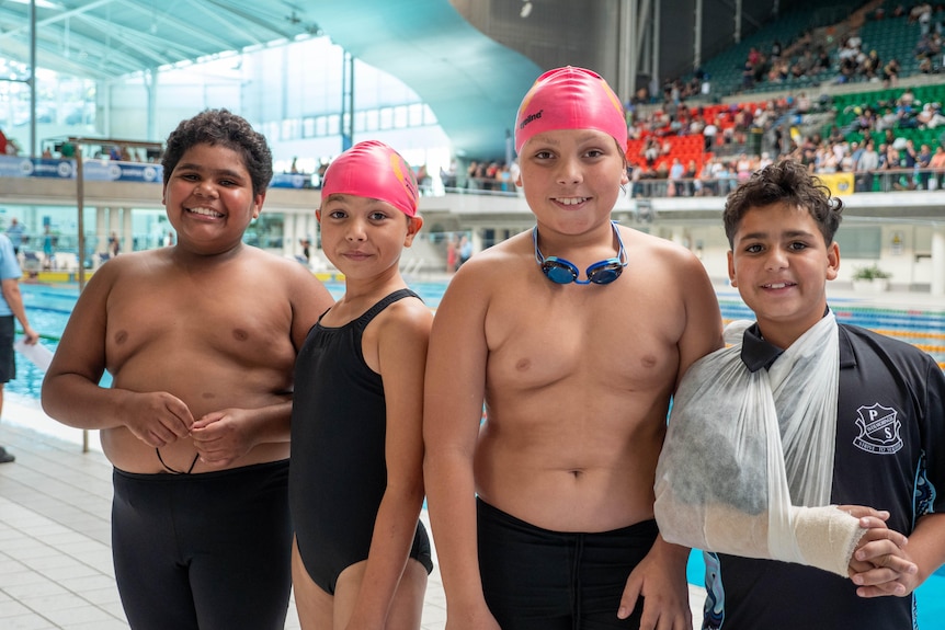 A group of four primary school aged kids smile standing next to a pool.