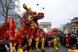 A line of men decked in yellow holding up a dragon on stick while being surrounded by a crowd