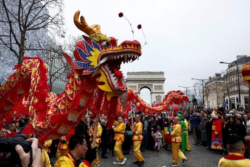 A line of men decked in yellow holding up a dragon on stick while being surrounded by a crowd