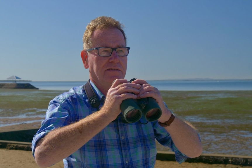 Robert Bush stands on the shore with binoculars.