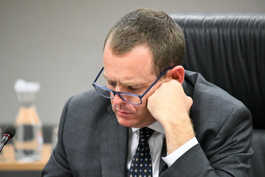 A man with short brown hair and glasses looks down at an iPad.