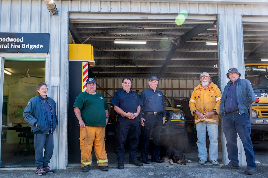Six people and one dog stand in front of a rural fire office.