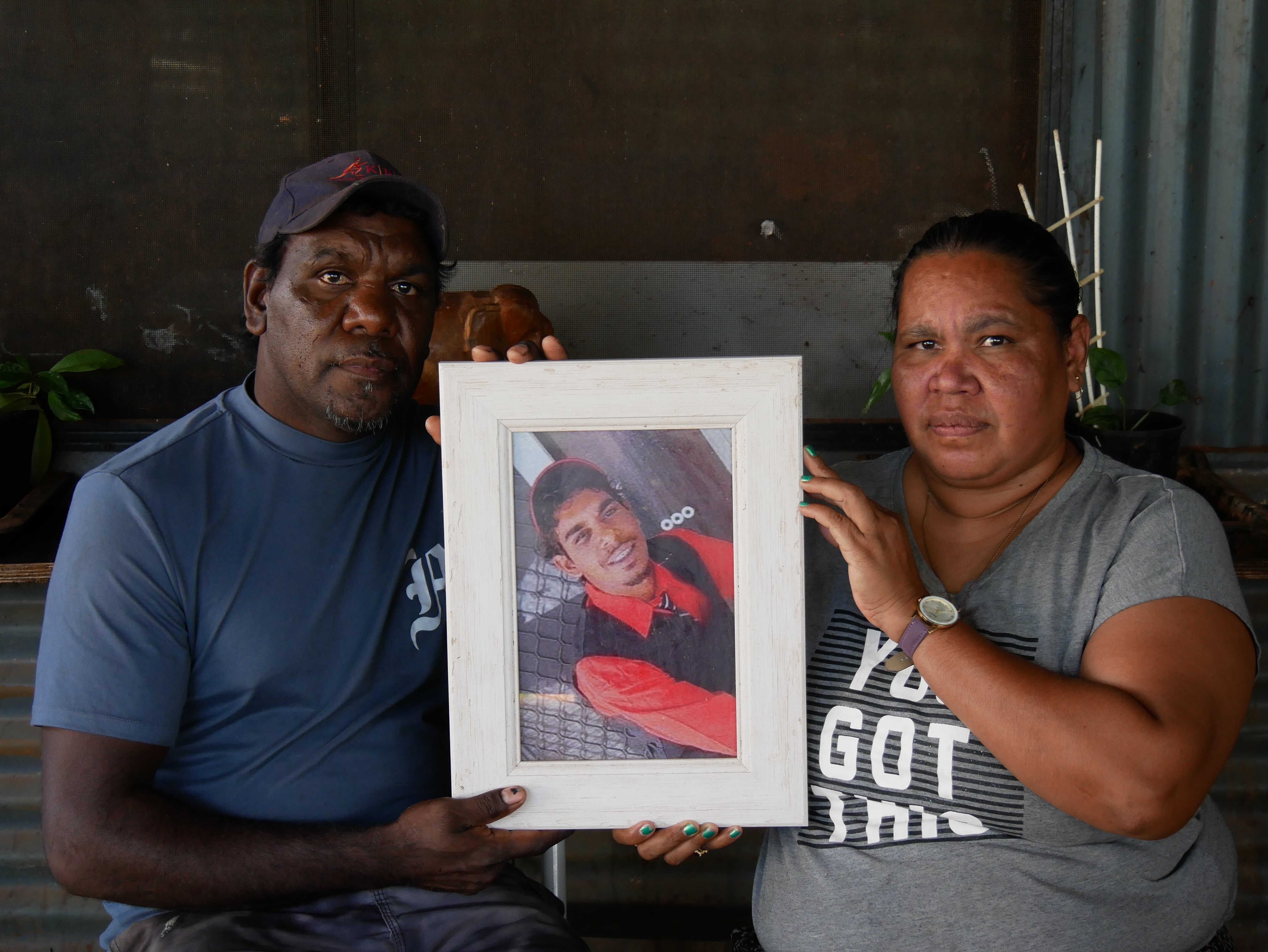An older man and woman holding a picture of a smiling young boy.