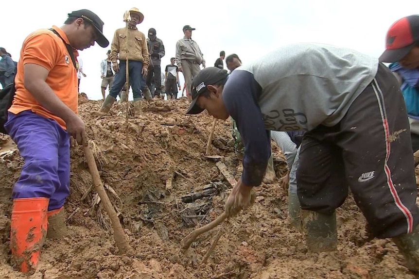 A group of men dig through the mud and debris