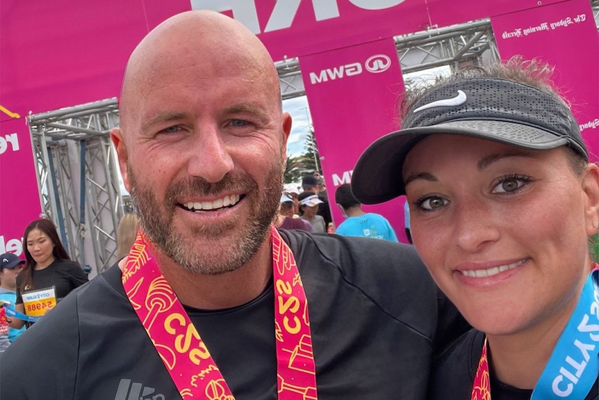 A man and woman stand next to each other in running clothes, smiling, with a medal around their neck.