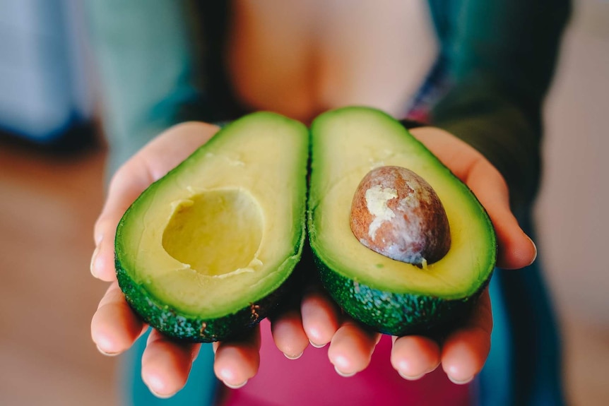 A woman holding two halves of the avocado.