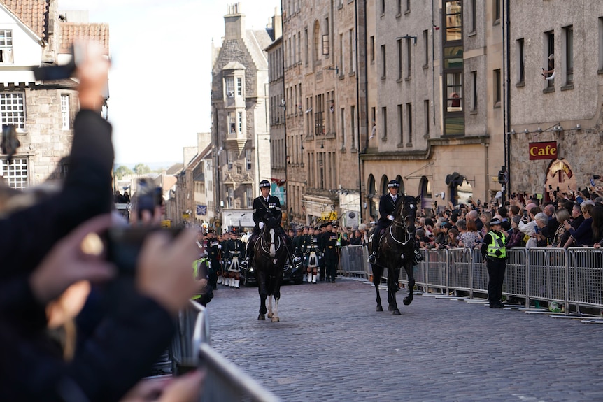 Two horse riders on a cobbled street surround by crowds