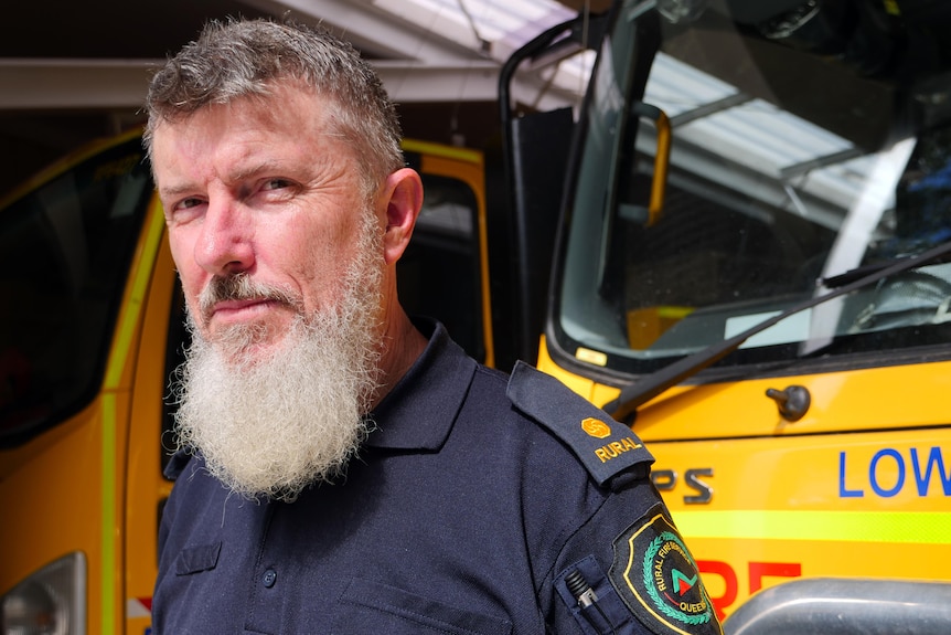 Bearded man stands beside a yellow fire truck.