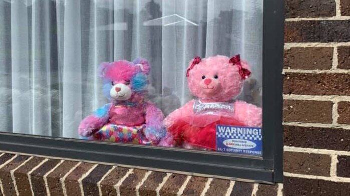 Two pink teddy bears sit in a window of a brick house.