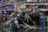 A motorcycle drives past a damaged tin roof and traffic signs caused by typhoon Soulik in Taipei