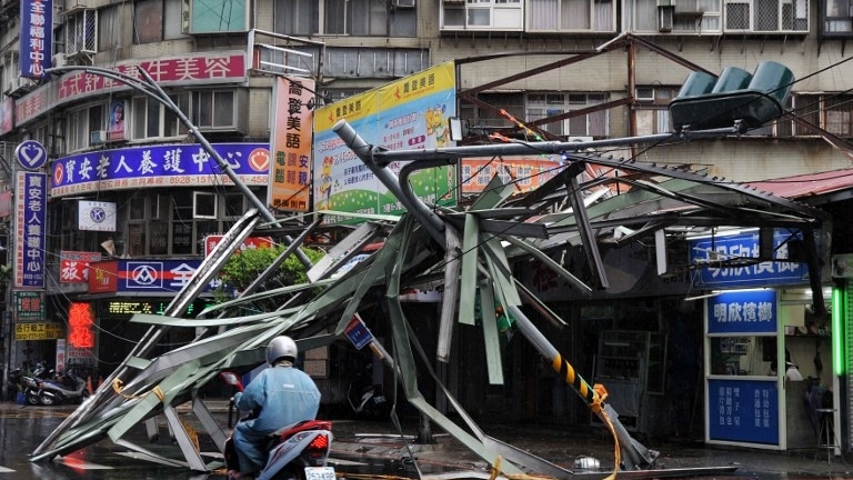 A motorcycle drives past a damaged tin roof and traffic signs caused by typhoon Soulik in Taipei