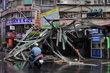 A motorcycle drives past a damaged tin roof and traffic signs caused by typhoon Soulik in Taipei